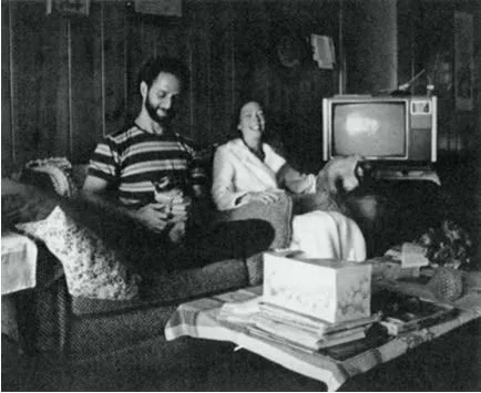 James McCarty e Carla Rueckert seduti sorridenti su un divano in un salotto, con un televisore alle loro spalle