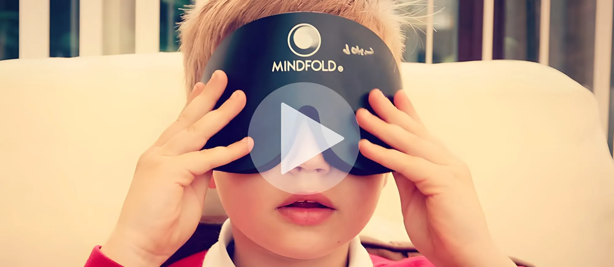 Bambino con una benda nera con la scritta Mindfold sugli occhi e le mani ai lati, con il simbolo di riproduzione di un video