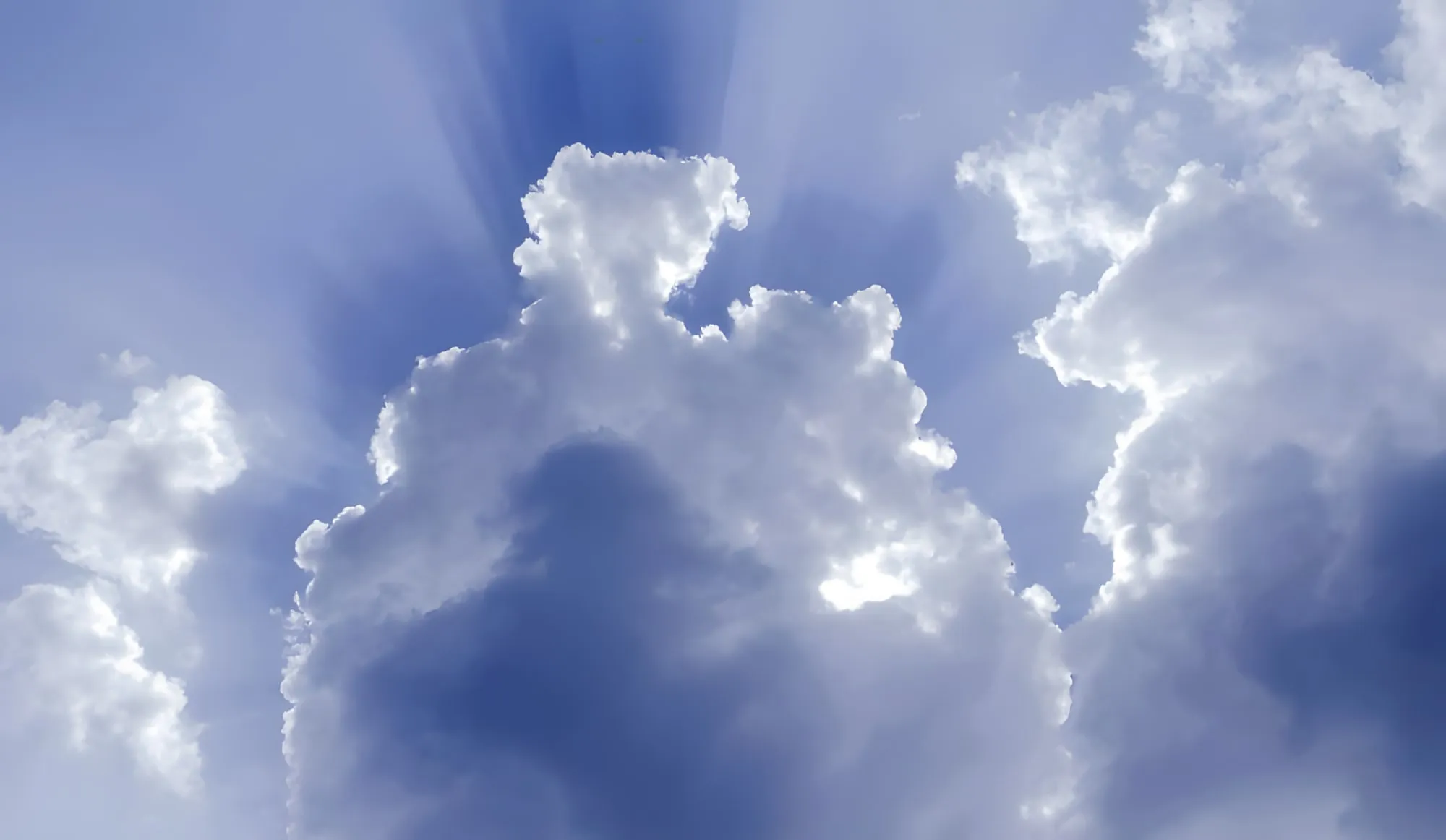 Cielo azzurro con grandi nuvole bianche da cui filtrano raggi di luce