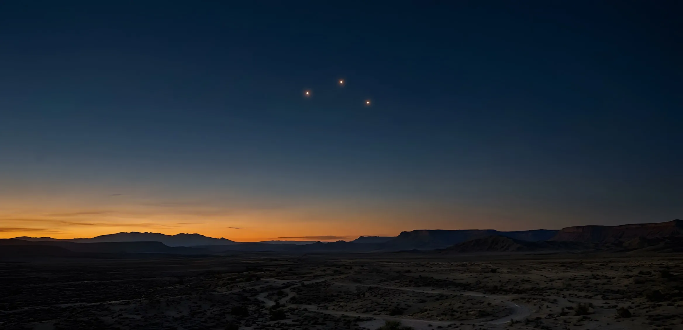 Tre piccole luci calde sospese in un cielo blu notte sopra un altopiano desertico, mentre l’ultimo bagliore ambrato si spegne all’orizzonte