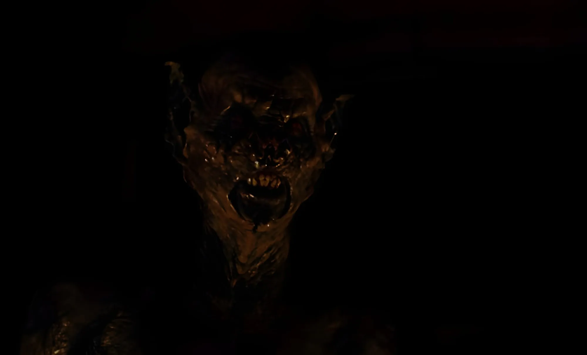 Figura demoniaca dal volto deforme e dalle orecchie a punta, emerge nel buio con la bocca aperta