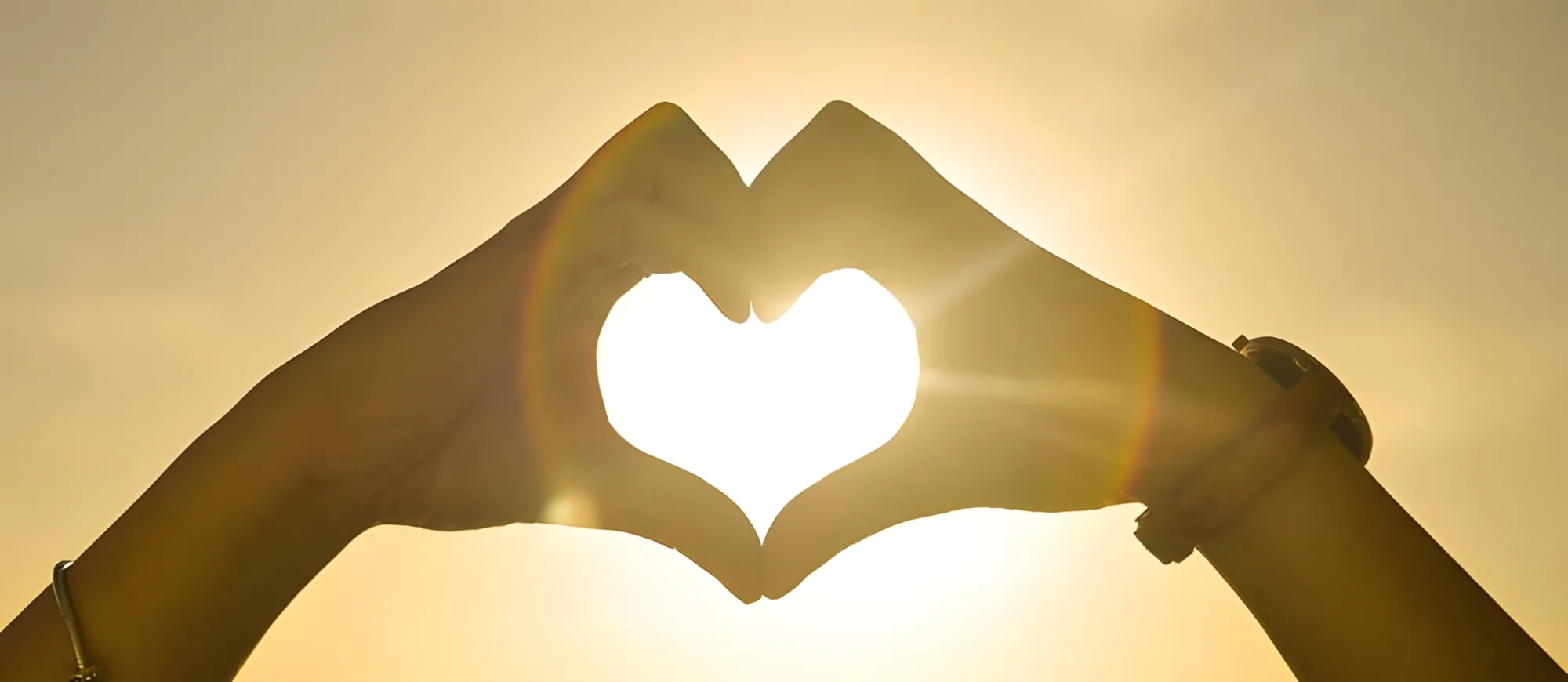 Due mani unite a forma di cuore che lasciano passare la luce del sole al tramonto