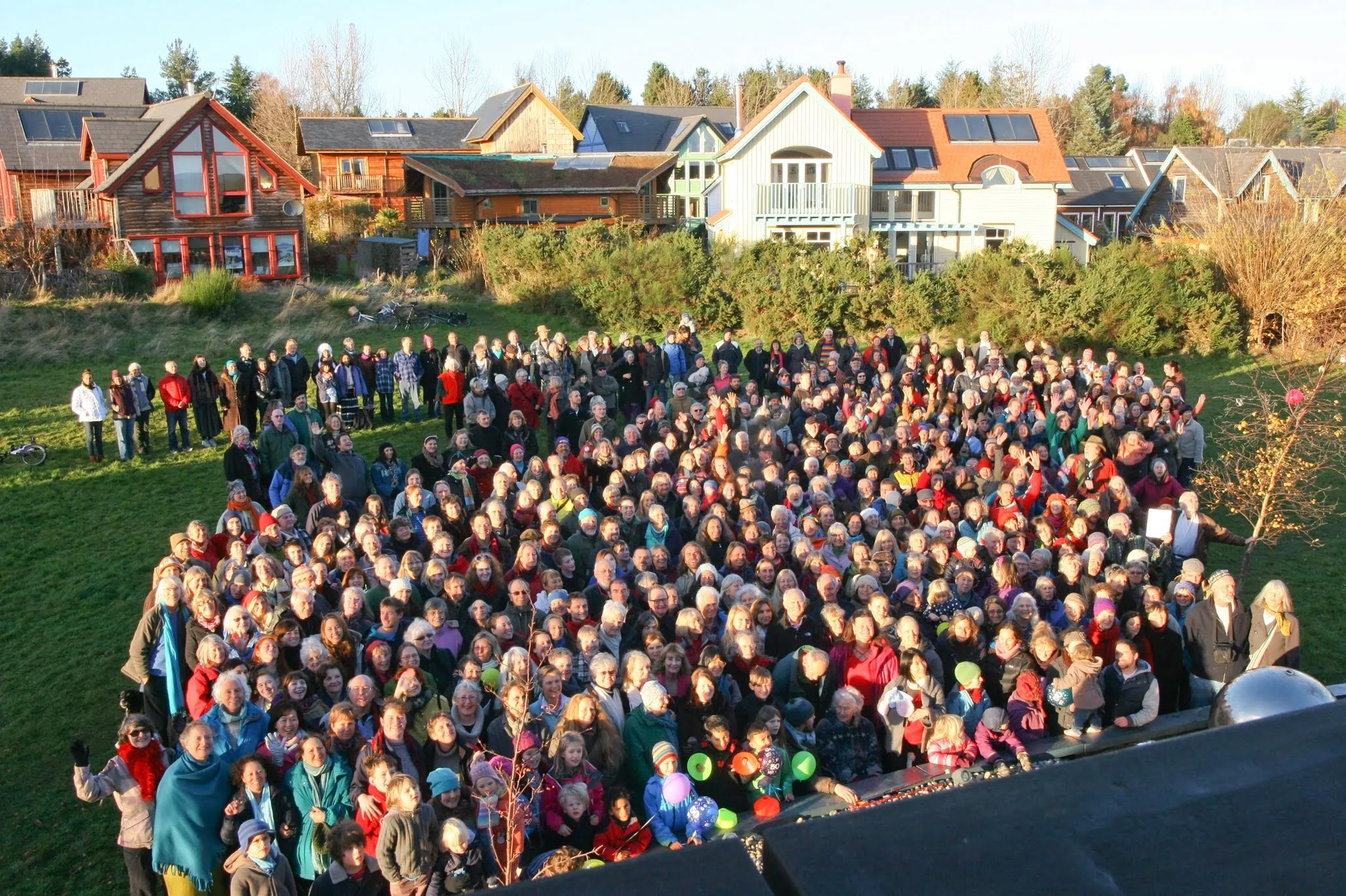 Foto dall’alto di centinaia di persone radunate su un prato davanti alle case ecologiche della comunità di Findhorn