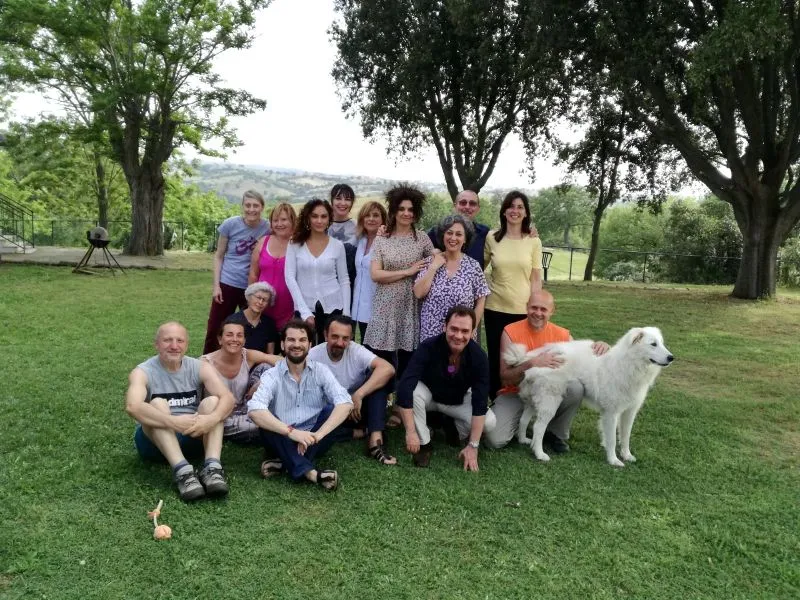 Foto di gruppo di circa quindici persone sorridenti sul prato di un giardino, con un grande cane bianco