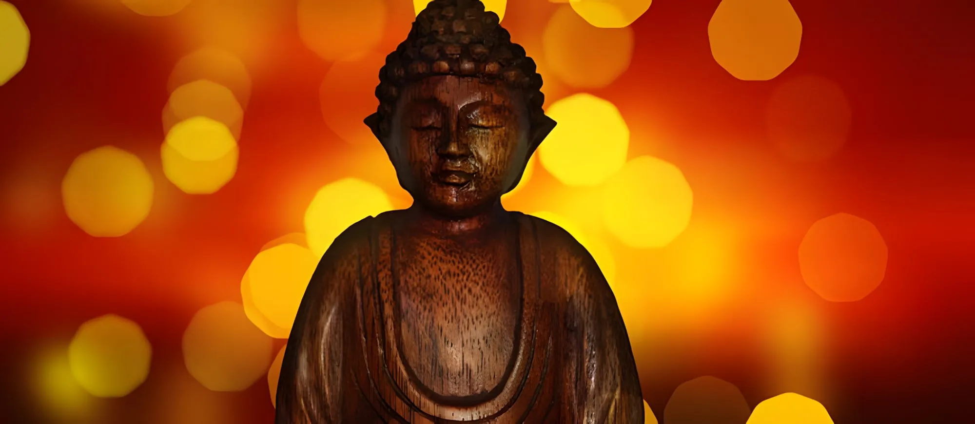 Statua di legno di un Buddha con gli occhi chiusi, su uno sfondo rosso e arancione di luci sfocate