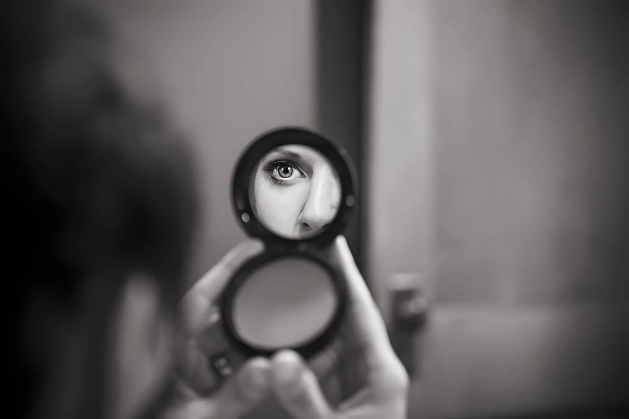 Autoritratto in bianco e nero: un occhio riflesso nello specchietto rotondo che una mano tiene aperto