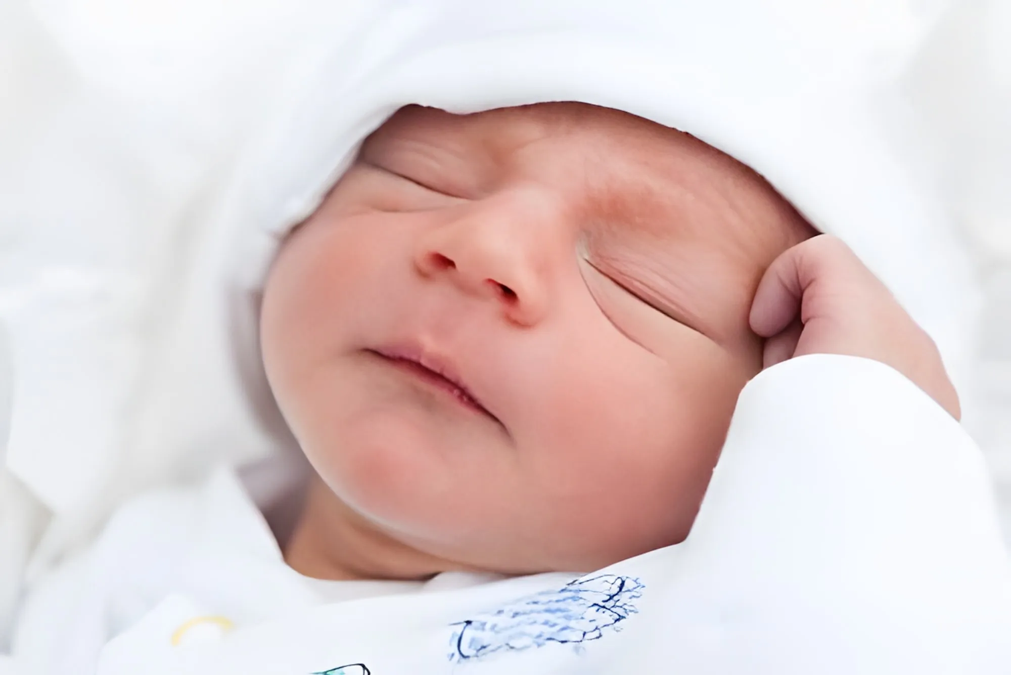 Neonato che dorme avvolto in un panno bianco, con una mano accanto al viso