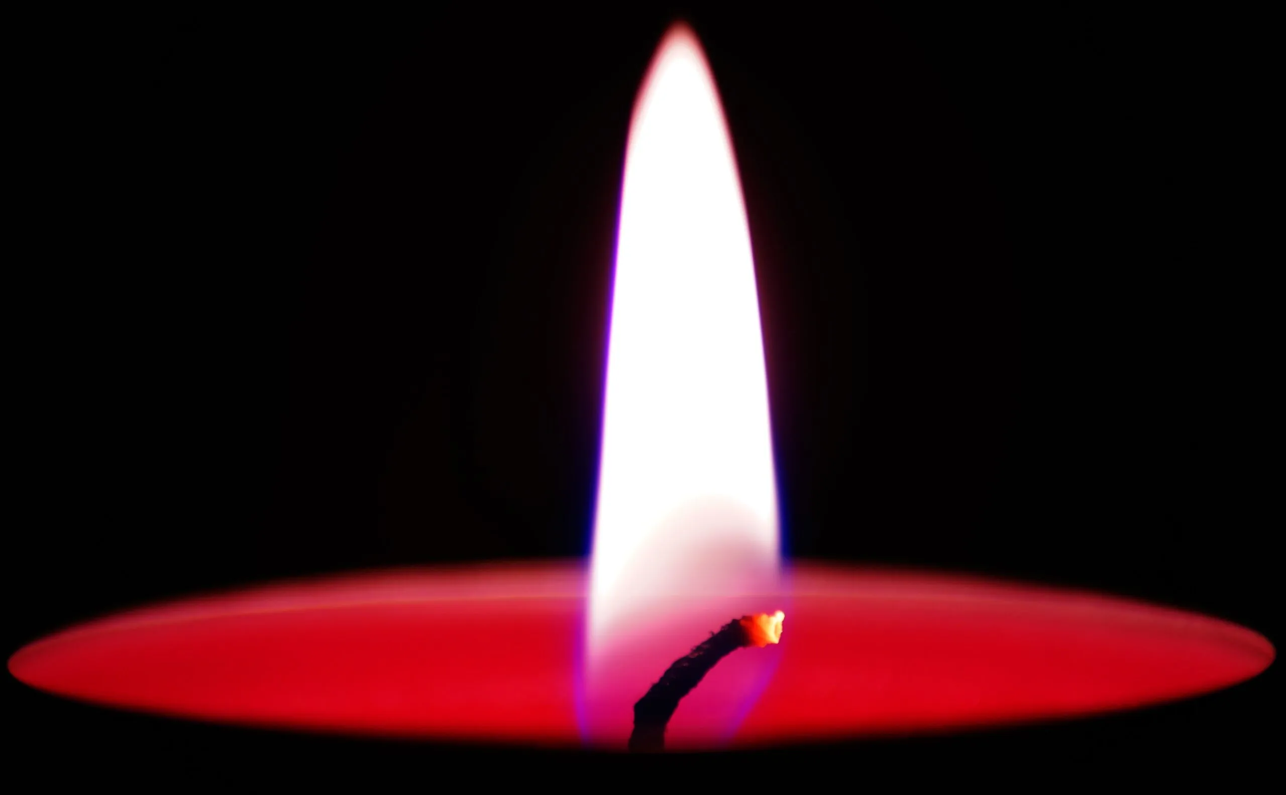 Primo piano della fiamma bianca di una candela rossa su sfondo nero