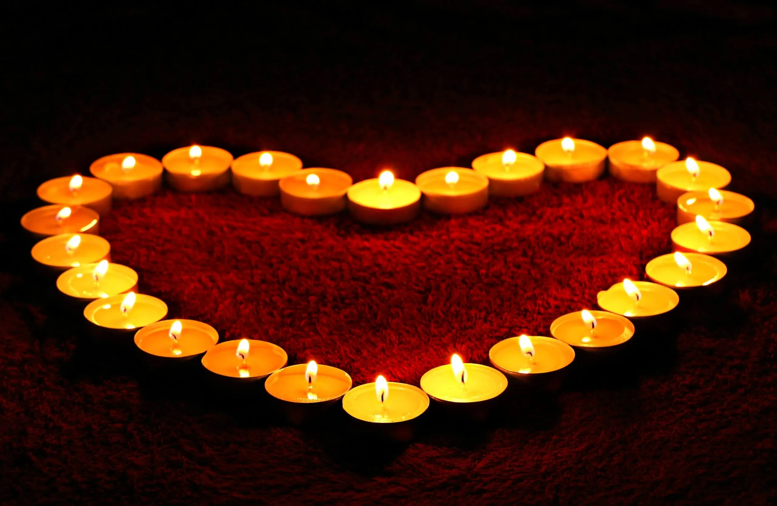 Candele accese disposte a forma di cuore su un tessuto rosso