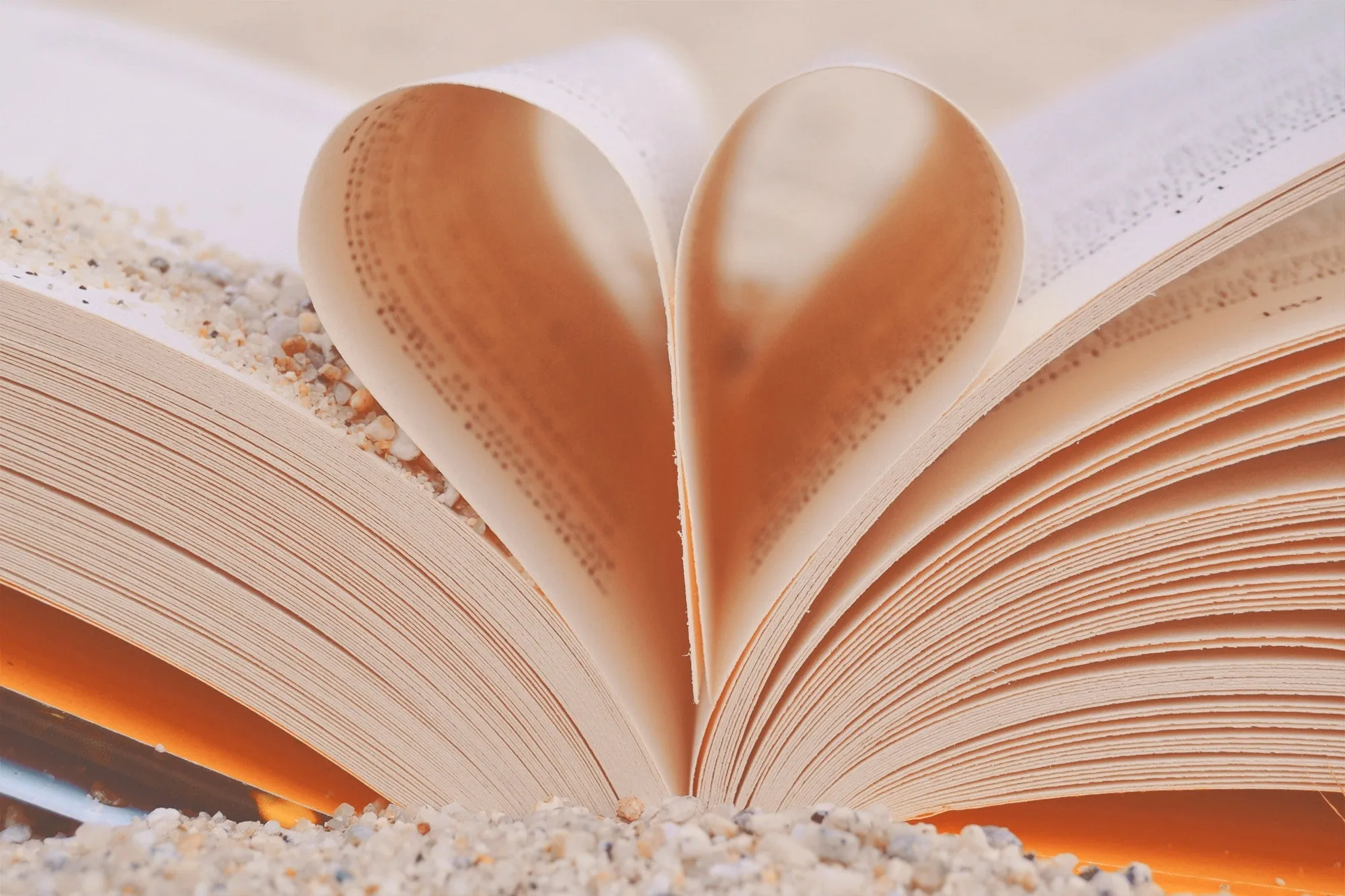 Libro aperto con due pagine piegate a forma di cuore, appoggiato sulla sabbia