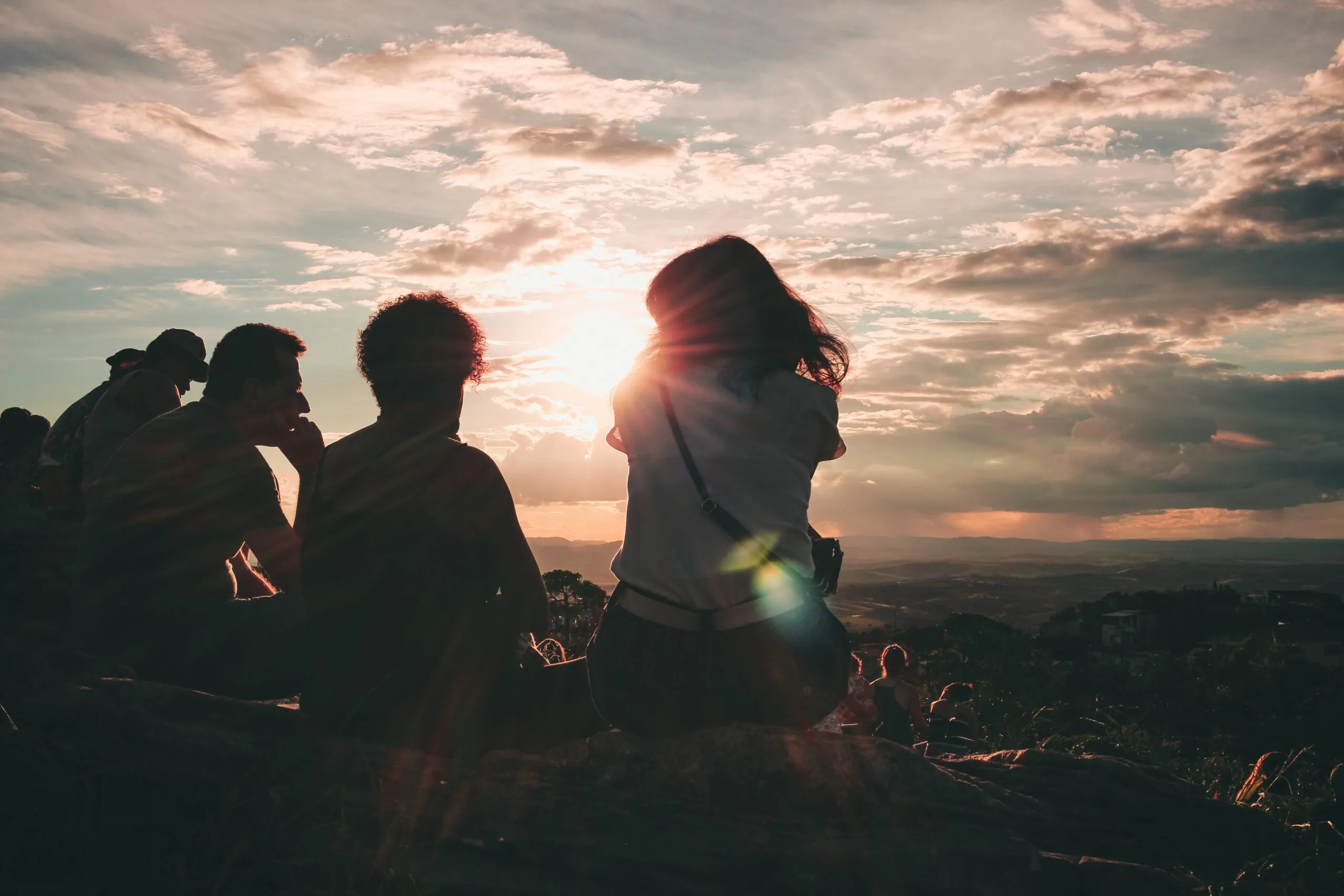 Tre persone sedute di spalle su una roccia guardano il tramonto sopra una vallata