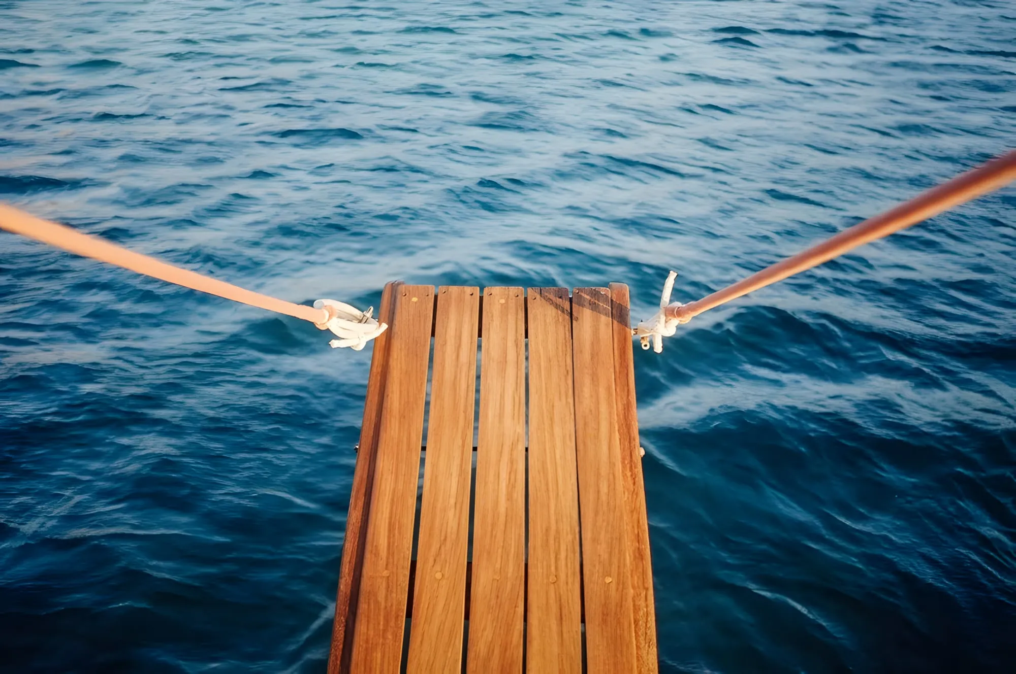 Trampolino di legno su un mare blu, tenuto da due corde, visto dall'alto