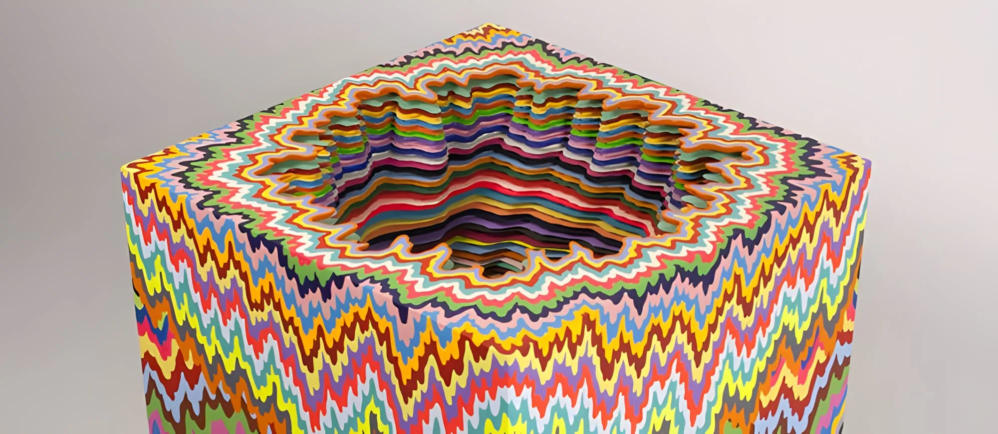 Scultura colorata a forma di cubo, con strati di linee ondulate di molti colori che formano una cavità al centro