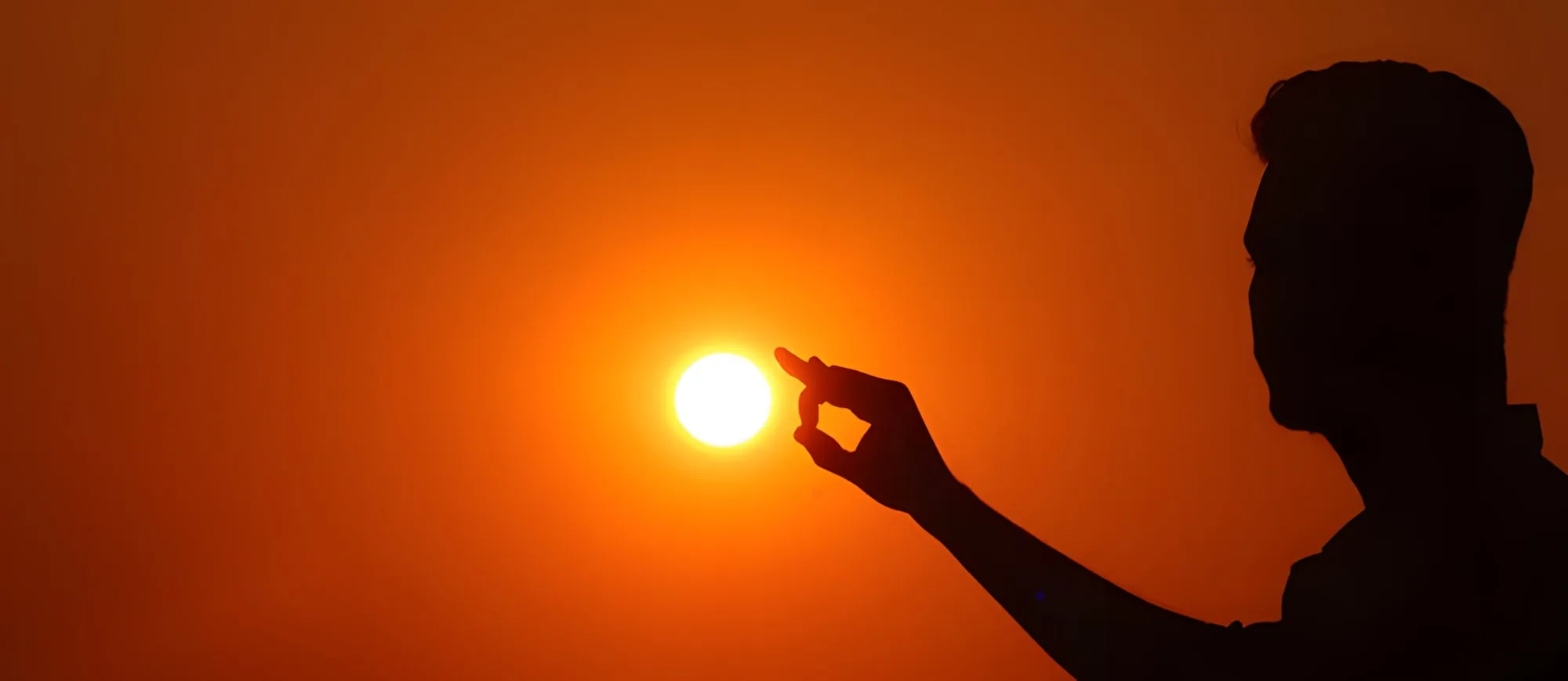 Sagoma di un uomo contro un cielo arancione, con le dita che sembrano reggere il sole