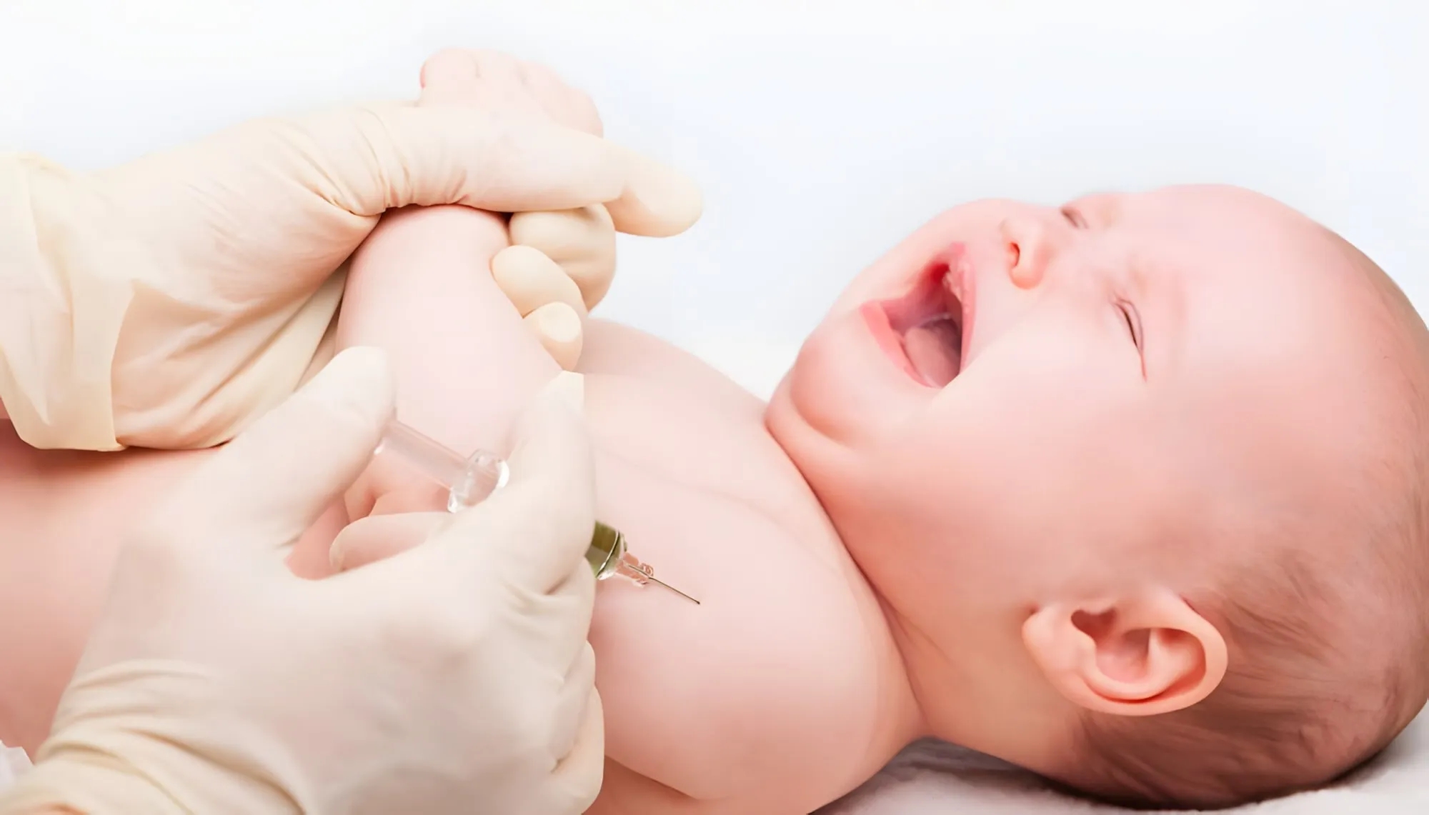 Neonato che piange mentre un’operatrice con i guanti gli fa un’iniezione nel braccio
